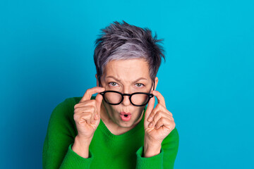 Elderly woman with surprised expression adjusting glasses against a vibrant blue background