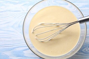 Whisk and bowl of dough on light blue wooden table, top view