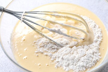 Whisk and bowl of dough on table, closeup