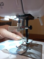 This is a close-up of a sewing machine in action. The needle is threaded and moves up and down as the fabric is fed through the machine. The person who sews guides the fabric with his hands.