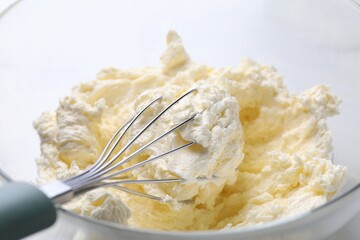 Bowl with whisk and whipped cream on white table, closeup