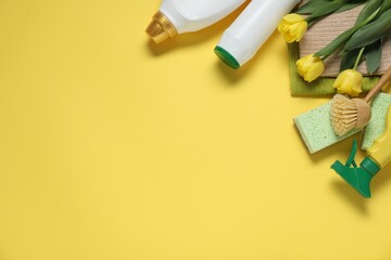 Spring cleaning. Detergents, supplies and tulips on yellow background, flat lay. Space for text