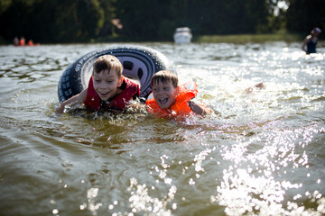 Młody chłopiec ubrany w pomarańczową kamizelkę asekuracyjną śmieje się i bawi na jachcie z rodzicami, bezpieczne wakacje na wodzie i jachcie © Katarzyna Krociel