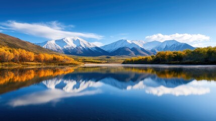 Obraz premium A serene landscape featuring majestic mountains reflected in a crystal-clear lake, surrounded by vibrant autumn foliage under a brilliant blue sky.