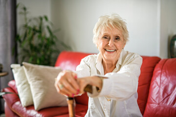 Beautiful senior woman sit on sofa with canes at home