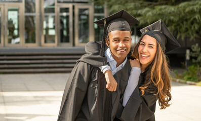 Two happy multiethnic college students celebrating graduation outdoors with copy space
