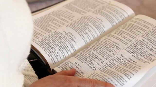 Christian woman is reading from open holy bible book while flipping its pages. Close-up. Biblical education and study concept.
