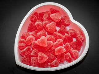 Close-up of heart-shaped red gummy candies in a white heart-shaped bowl on a dark background.