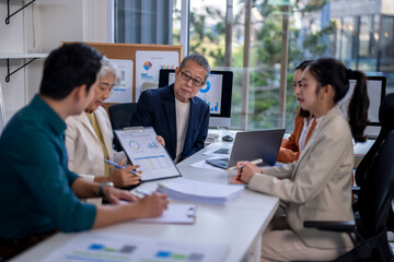 A group of people are sitting around a table with papers and laptops