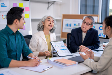 Fototapeta premium A group of people are sitting around a table with a woman holding a presentation