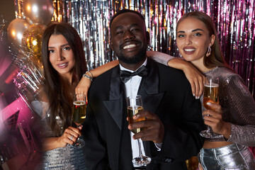 Three friends dressed elegantly, celebrating an event with drinks, sparkling decorations, and...