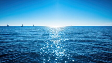 A serene ocean view with sailboats against a bright blue sky and shimmering water.