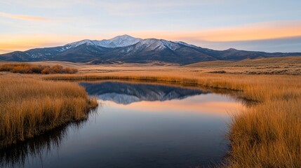 Tranquil mountain lake reflection at sunset with snow capped peaks and golden dry grass in rural wilderness landscape. Scenic nature view in american west with copy space