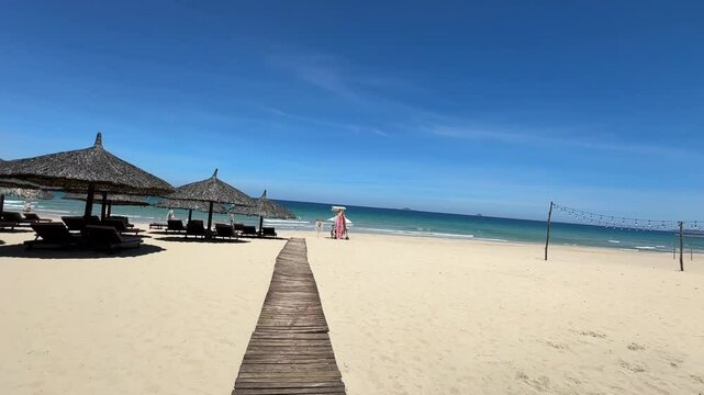 Experience a breathtaking aerial journey over a pristine tropical beach. The camera gracefully pulls back to reveal a captivating scene featuring a long wooden boardwalk, soft white sands, and charmin