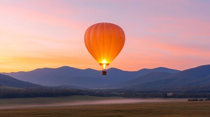 Fototapeta premium Orange hot air balloon glowing at sunrise over misty mountain valley landscape with purple sky. Adventure travel and peaceful morning serenity in nature scenery with copy space