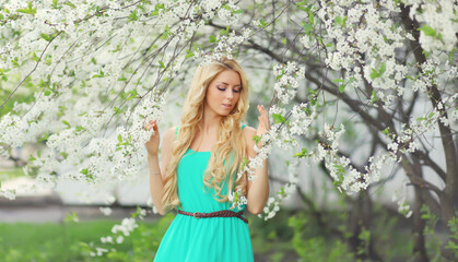 Beautiful blonde young woman in spring blooming garden on a sunny day against flowers trees