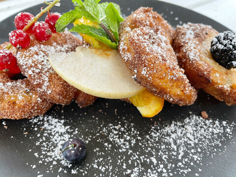 Apple Fritters on a dark plate with sugar and fruits