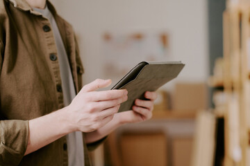 Fototapeta premium Person using digital tablet while standing in modern office setting, focusing on work-related tasks with shelves in background