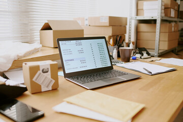 Workspace with open laptop showing inventory system on screen, surrounded by packing boxes on...