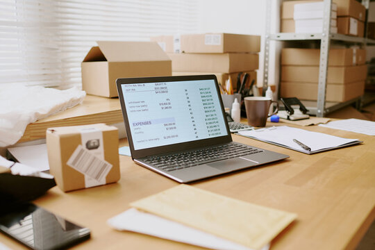 Workspace with open laptop showing inventory system on screen, surrounded by packing boxes on shelves and desk enhancing productivity in office setting
