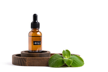 Essential oil in glass bottle on wooden plate with green leaves isolated on white background.