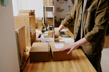 Person labeling packages in warehouse workspace, preparing shipments for dispatch, ensuring...