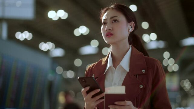 Stressed young asian businesswoman traveler confused missing flight and using smartphone to check flight information and holding passport and boarding pass standing in the airport terminal.
