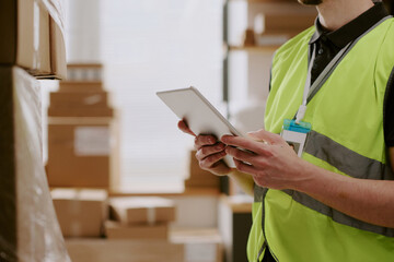 Worker managing inventory in warehouse using a handheld device for efficiency surrounded by stacked...