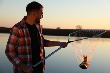 Fisherman holding fishing net with catch at riverside