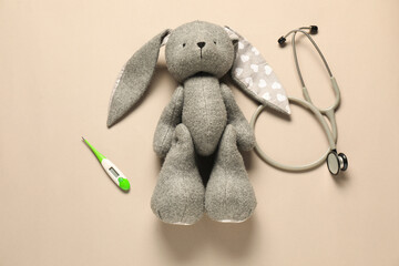 Pediatrics concept. Toy bunny with stethoscope and thermometer on beige background, flat lay