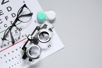 Glasses, trial frame, lenses and vision test chart on gray background, flat lay. Space for text