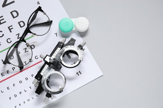 Glasses, trial frame, lenses and vision test chart on gray background, flat lay. Space for text