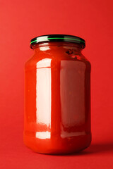 Ketchup in glass jar on red background