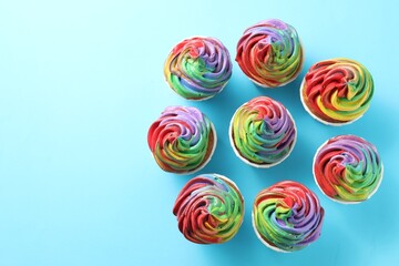 Delicious cupcakes with colorful cream on light blue background, flat lay. Space for text