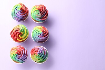 Delicious cupcakes with colorful cream on violet background, flat lay. Space for text
