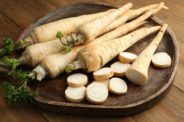 Whole and cut fresh parsley roots on wooden table, closeup