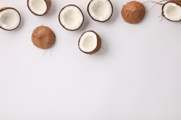 Halves of fresh coconuts on light background, flat lay. Space for text