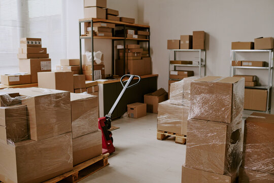 A collection of brown cardboard boxes varying in size stacked on wooden pallets and shelves in a warehouse environment