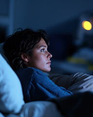 Obraz premium Jeune femme pensive allongée dans un lit sombre, regardant au loin