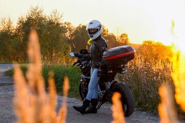 A girl in full motorcycle gear and a helmet with a pigtail stands on the side of the road....