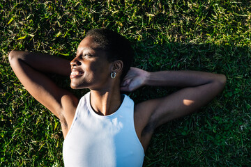 Young black woman relaxing lying on green grass smiling with hands behind head