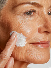 A close-up of an older woman with smooth, radiant skin applying anti-aging cream to her cheek, highlighting skincare and beauty routines