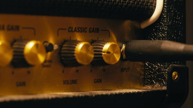Close-up of plugging a jack into a guitar amplifier and turning up the volume knob, live concert show, playing music on guitar tube amplifier.
