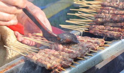 hand of chef with a brush soaked in oil and salt is brushing the mutton skewers called ARROSTICINI...