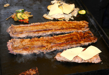 pork sausages and mixed vegetables cooking on the hot griddle with some slices of cheese