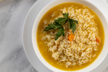 Bowl of soup with a spoon and spoon on a wooden table, steam rising, petals scattered around.