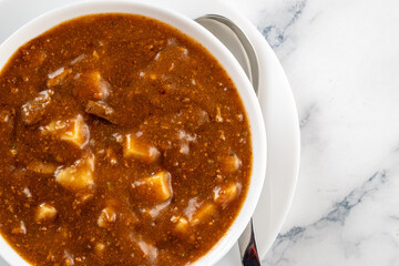 Bowl of chili soup with a spoon, steam rising. Garnished with fresh cilantro & a slice of lime. Rustic wooden table & cozy ambience in soft lighting.