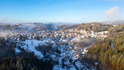 In a serene winter landscape, a stone railway bridge stands proudly in Smrzovka, Czechia. A blanket of snow covers the quaint village and surrounding trees, creating a picturesque scene.