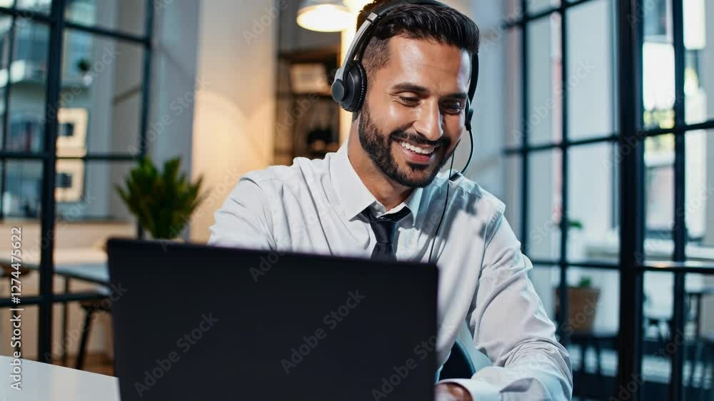Poster professional video call setting with a man in a headset, smiling at a laptop. shot from a low angle 
