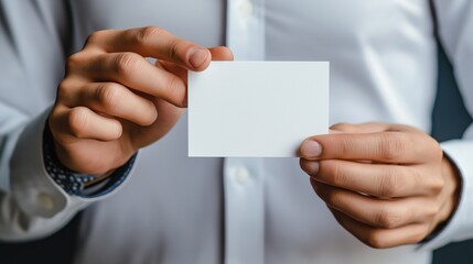 A man is holding a white business card in his hand. The card is blank, which suggests that it is a new card or a card that has not been filled out yet